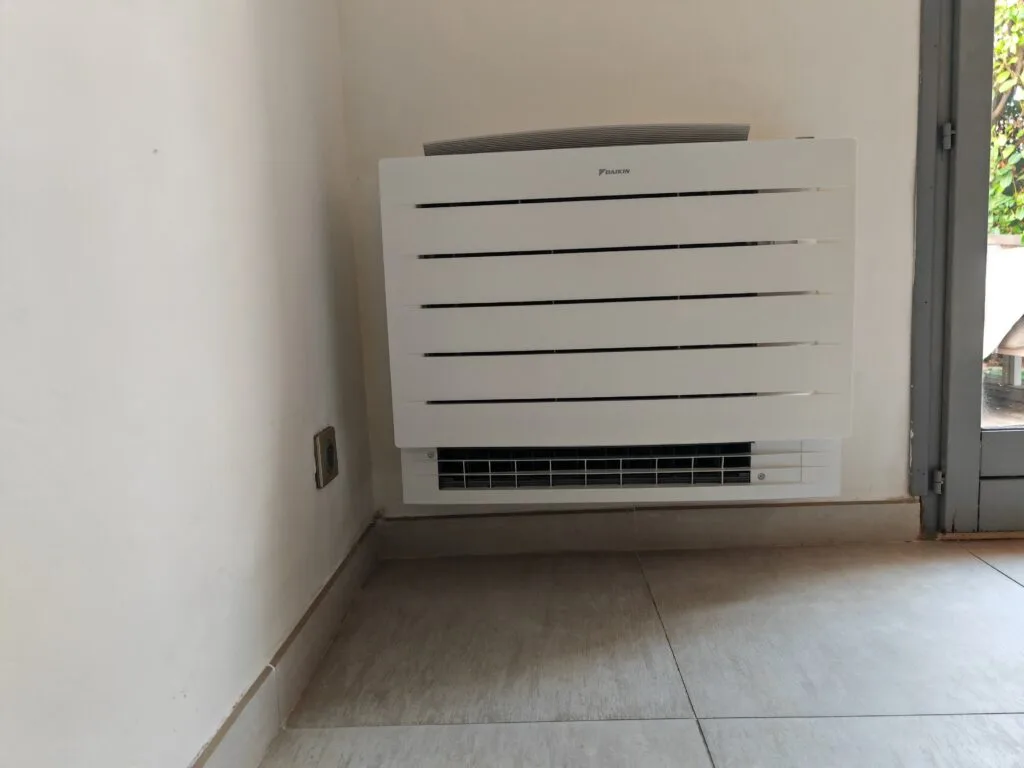 Console de climatisation Daikin posée en bas de mur, à côté d’une porte-fenêtre