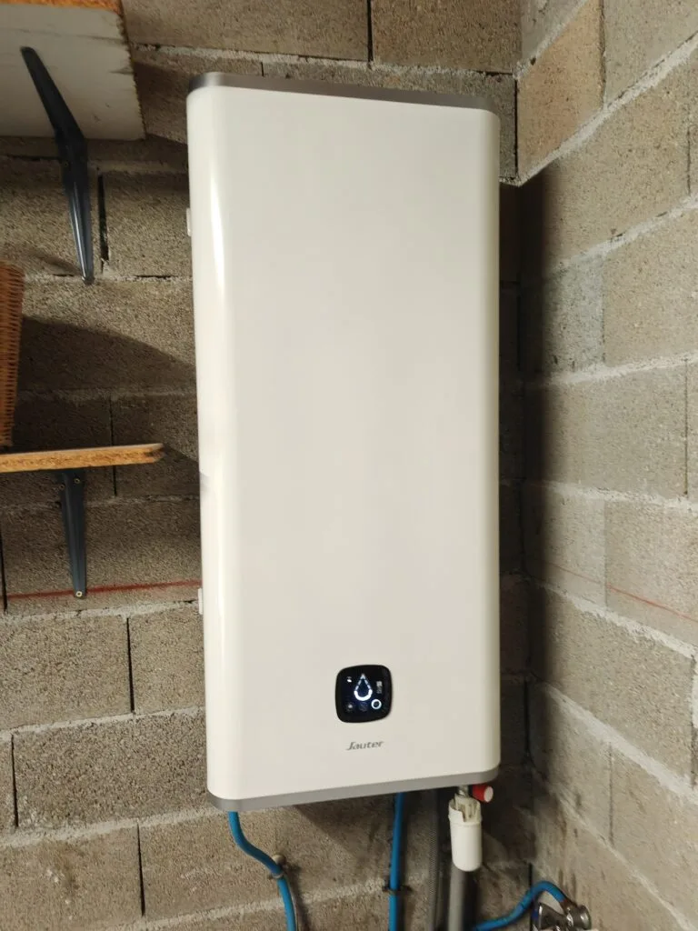 Chauffe-eau électrique plat Sauter posé au mur d’un garage, arrivées d’eau et groupe de sécurité en dessous