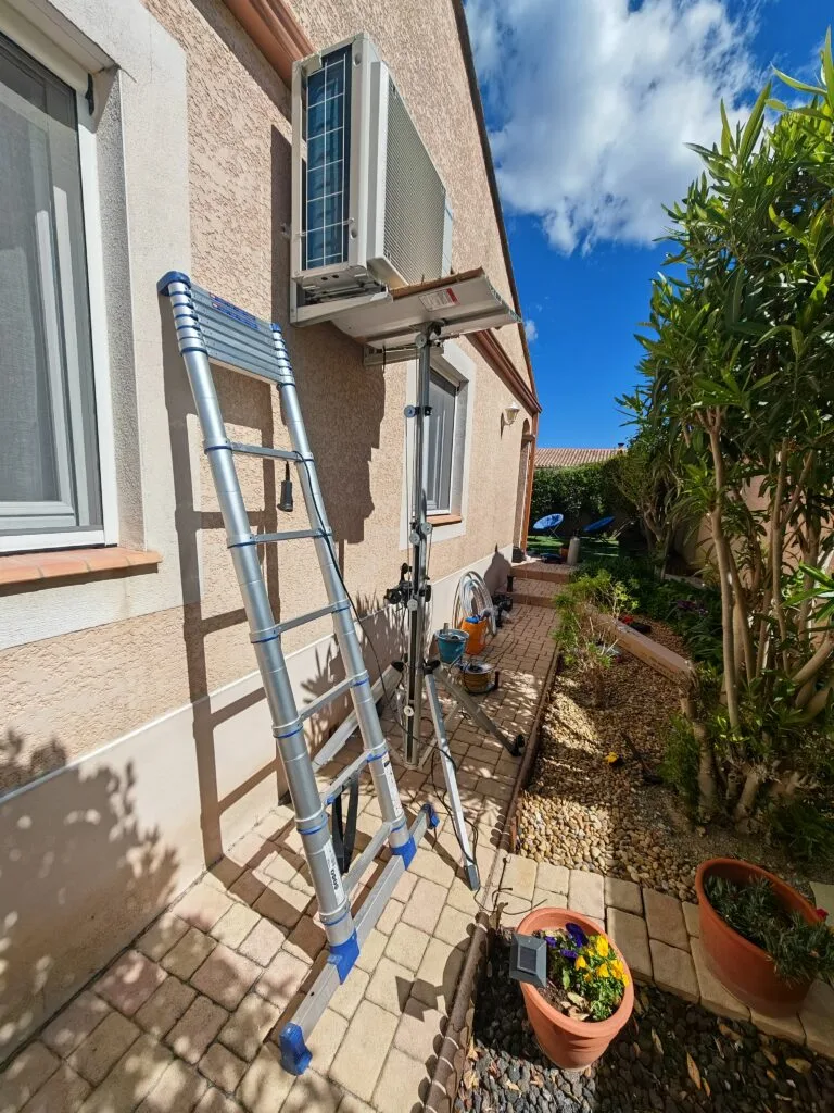 Unité extérieure de climatisation hissée au lève-matériaux jusqu’à sa console, contre la façade d’une maison