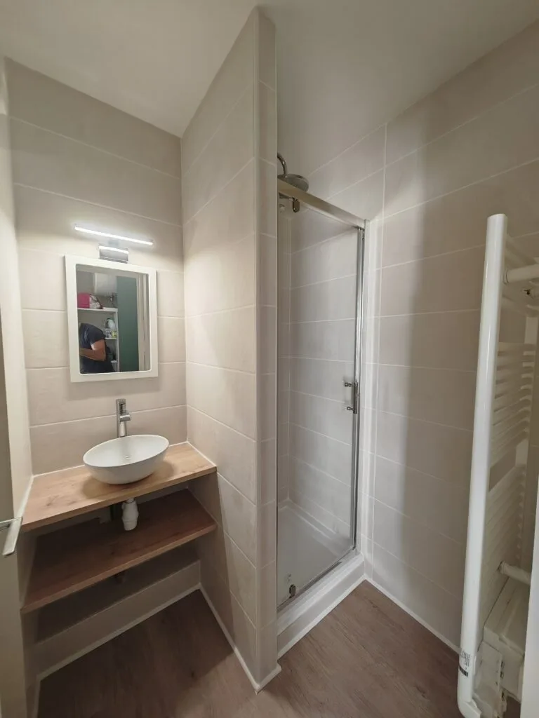 Salle d’eau rénovée avec vasque à poser sur plan en bois, cabine de douche et sèche-serviettes