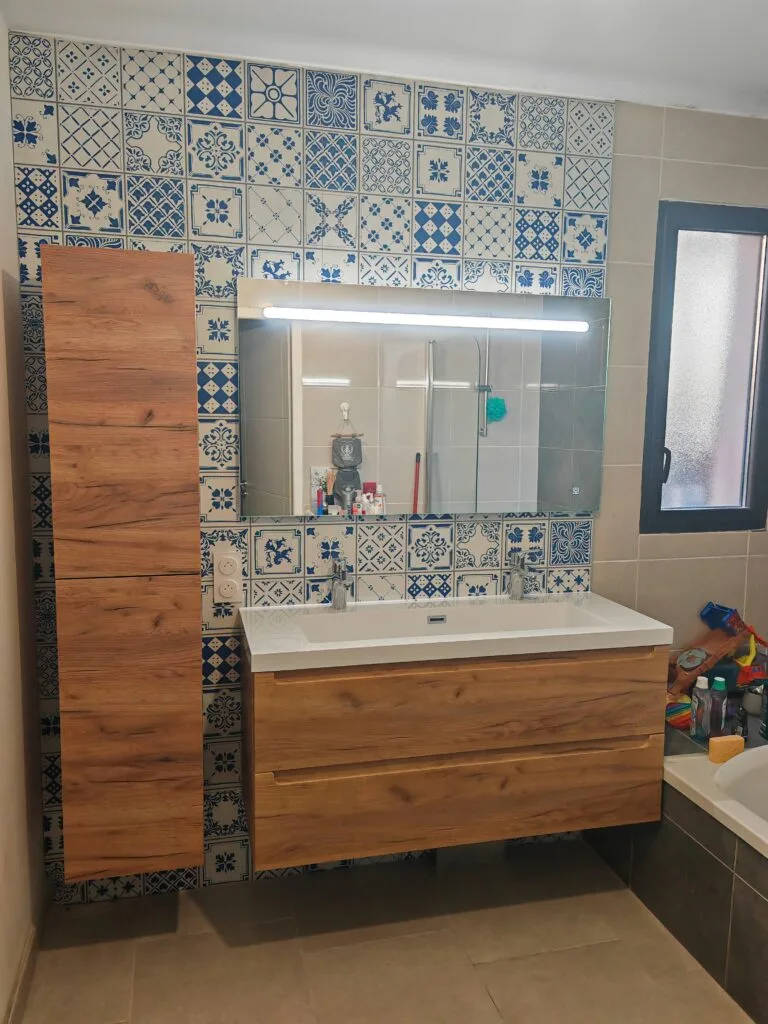 Salle de bains rénovée : meuble double vasque en bois, colonne de rangement et faïence à motifs bleus