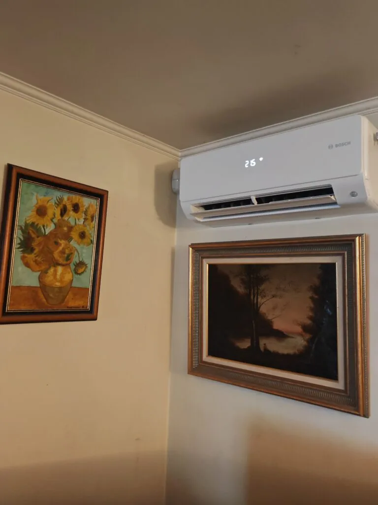 Split mural de climatisation installé dans l’angle d’un séjour, au-dessus de tableaux