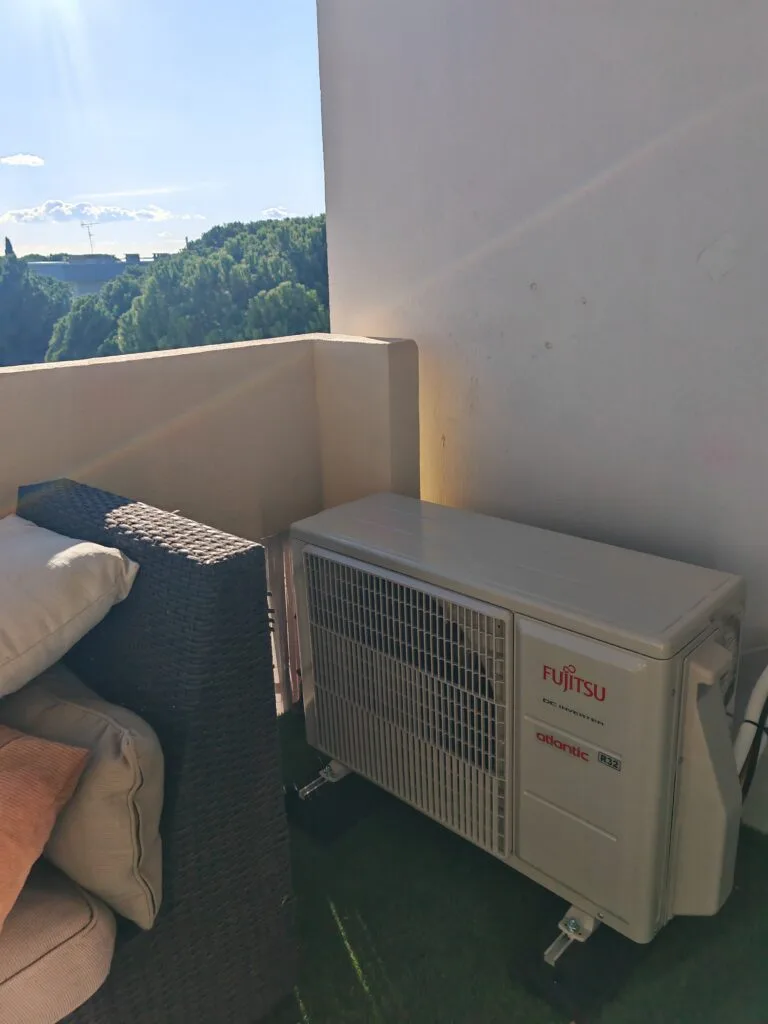 Unité extérieure de climatisation posée sur pieds au sol d’un balcon d’appartement