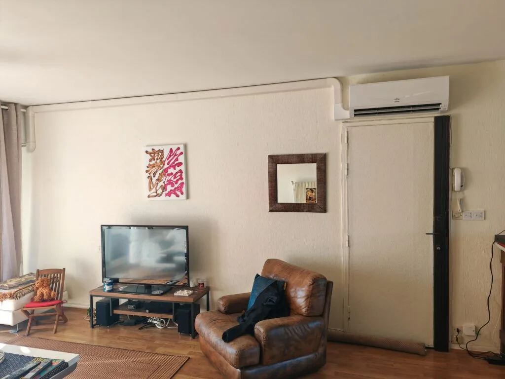 Split mural de climatisation posé en haut d’un mur de séjour, au-dessus d’une porte