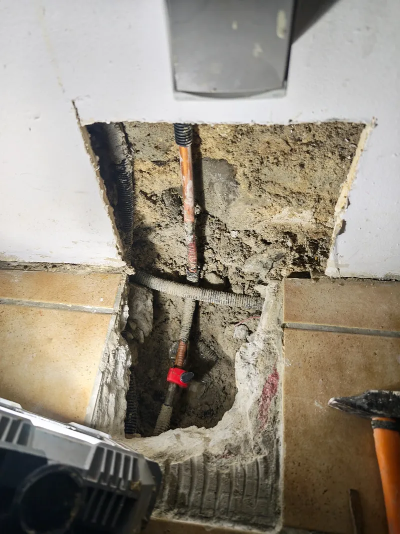 Avant : tube en cuivre encastré rongé par la corrosion, avec réparation de fortune, dans le mur et le sol ouverts